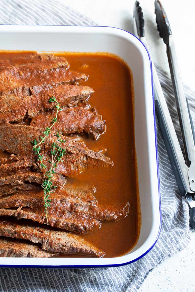 Braised beef brisket in a rectangular serving dish, with kitchen tongs on the right