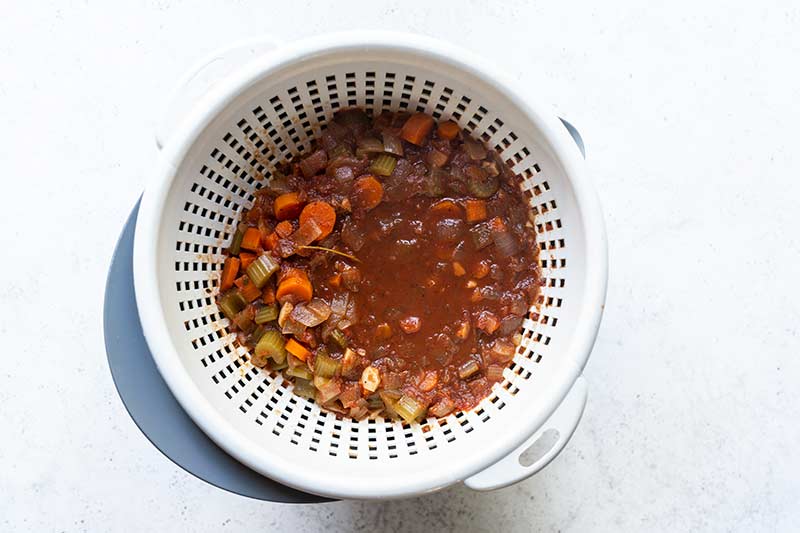 a bowl topped with a colander, filled with braising liquid to strain out the solids