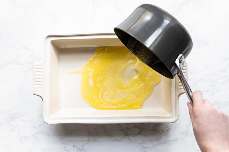 pouring melted butter from a saucepan into a casserole dish