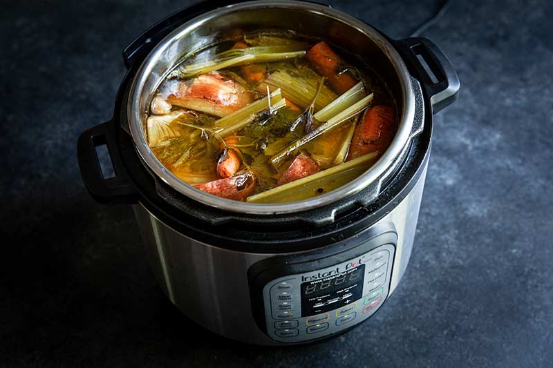 Lid removed from a pressure cooker showing cooked, unstrained stock
