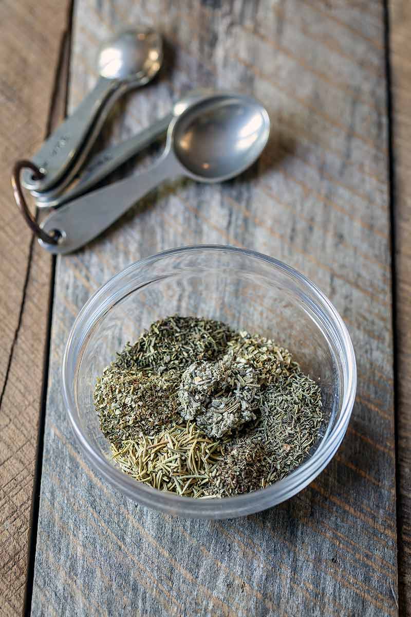 All spices for Italian Seasoning Recipe in a bowl next to measuring spoons