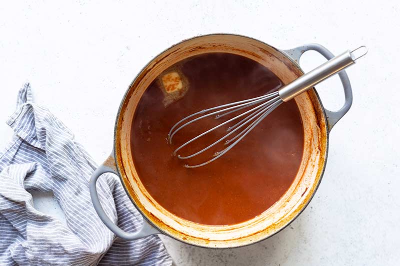 Reduced Jewish brisket sauce in a dutch oven with a melting pat of butter and a whisk