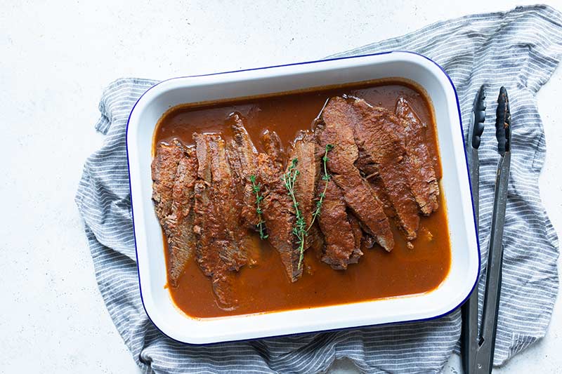 Braised beef brisket recipe in a rectangular serving dish, with kitchen tongs on the right