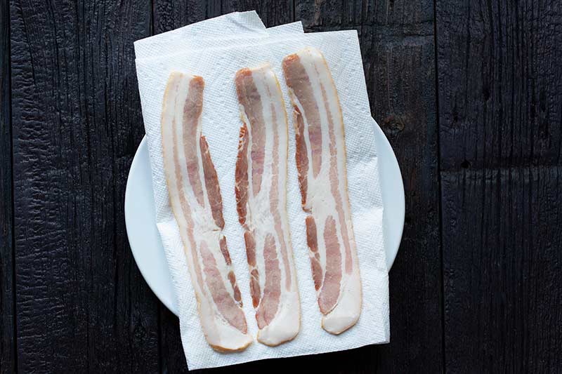 Raw bacon on a paper towel-lined plate