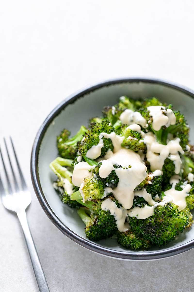 broccoli side dish covered in cheesy white sauce in a bowl next to a fork