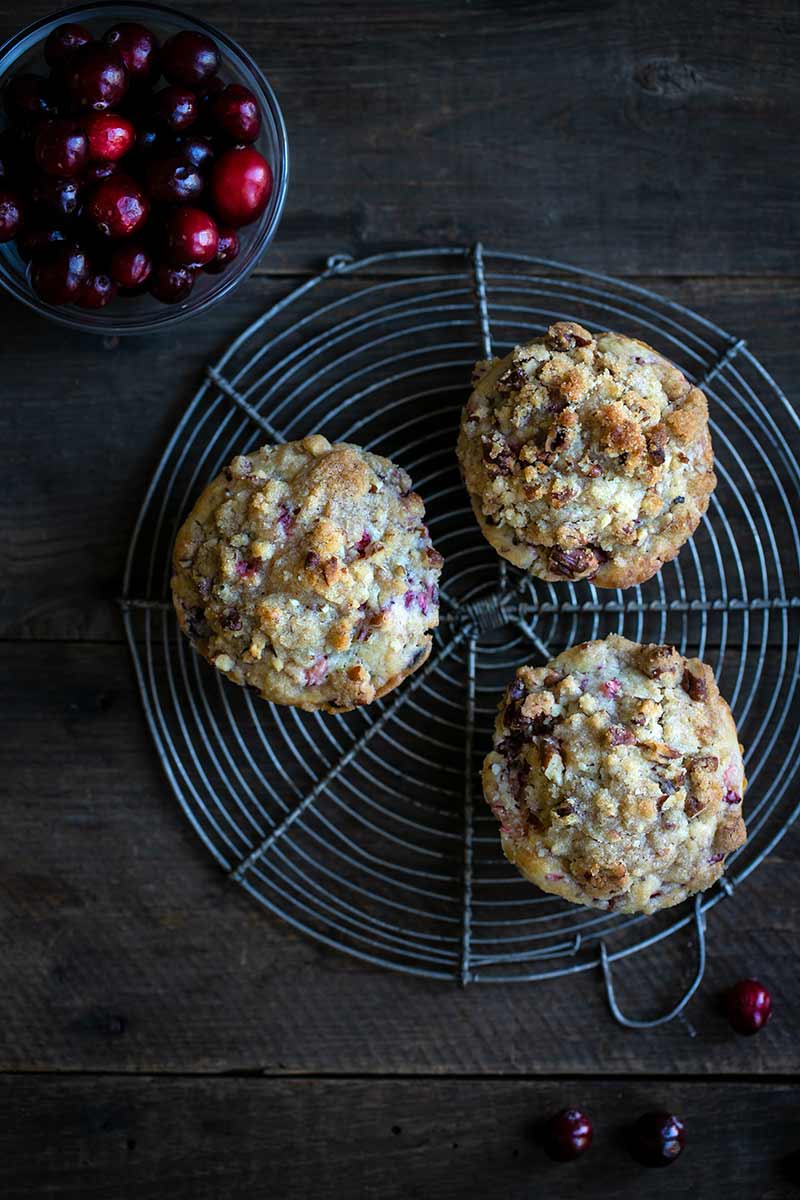 Overhead shot of three fresh cranberry muffins on a round cooling rack