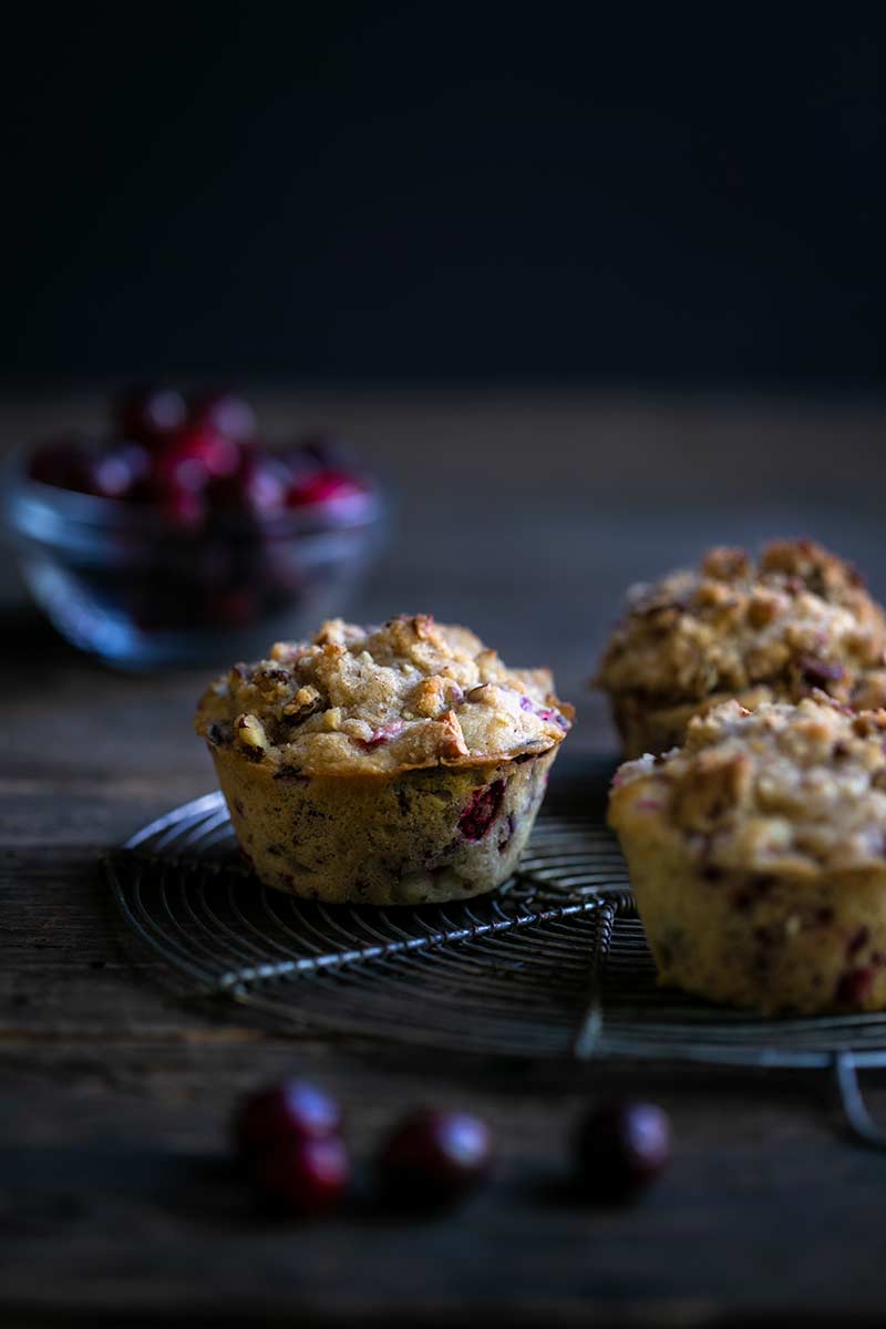 Three cranberry pecan streusel muffins on a cooling rack with cranberries in the background