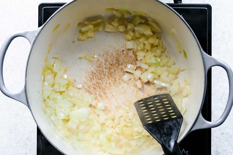 Chopped onions browning in an enameled Dutch oven with a spatula