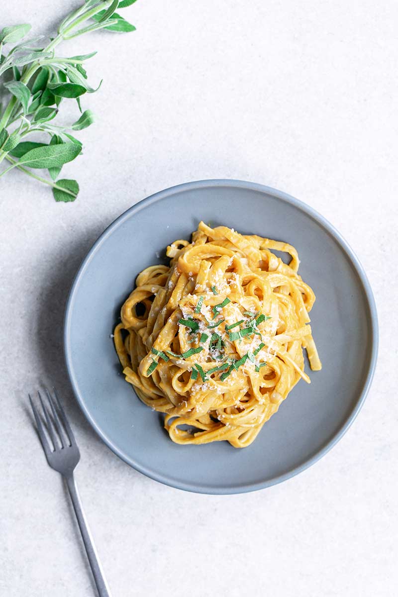Creamy pumpkin pasta recipe on a blue plate, topped with sage and parmesan cheese