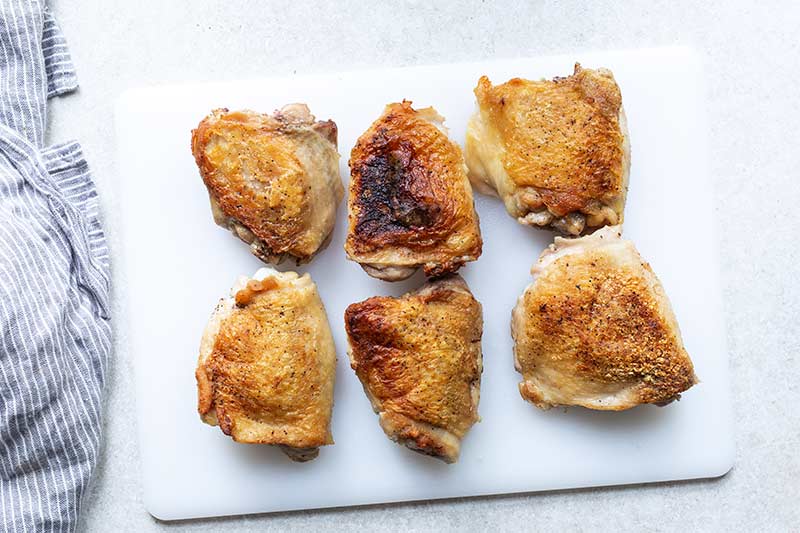 seared chicken thighs with brown crispy skin on a clean cutting board after cooking