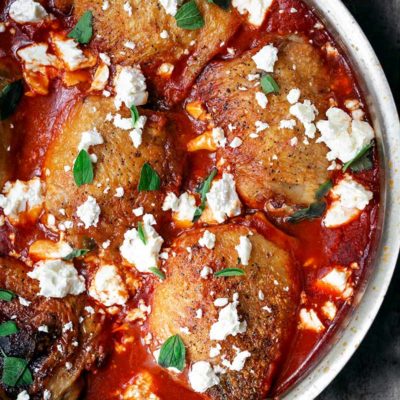 A closeup photo of crispy chicken thighs with spiced tomato sauce in a skillet