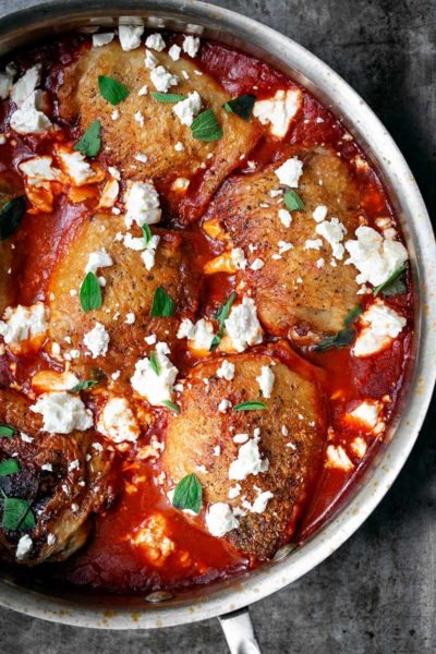 A closeup photo of crispy chicken thighs with spiced tomato sauce in a skillet