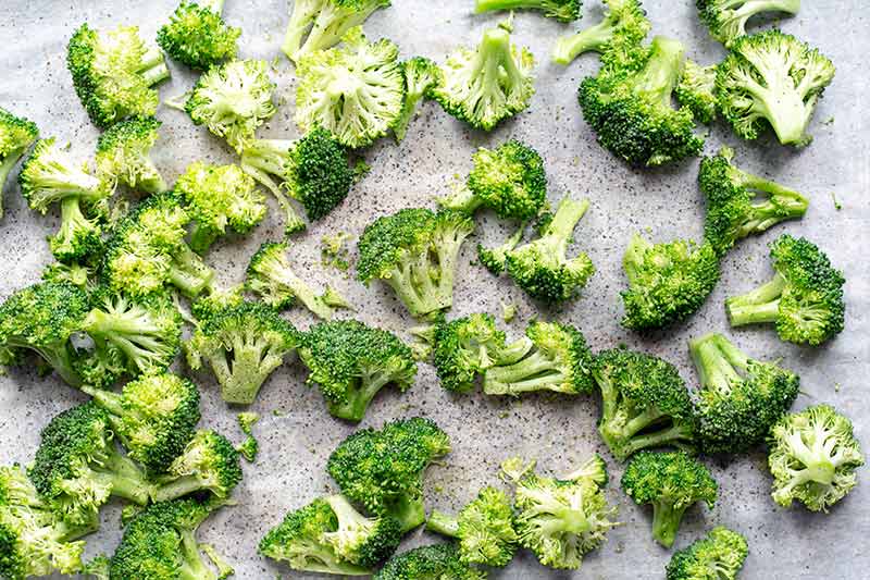 Raw broccoli florets on a sheet pan tossed with olive oil, salt and pepper