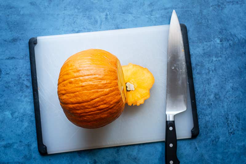 A pumpkin laying on its side on a cutting board with the stem removed.