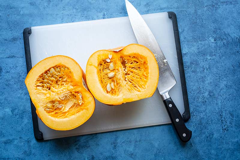 Two pumpkin halves laying flesh side up on cutting board