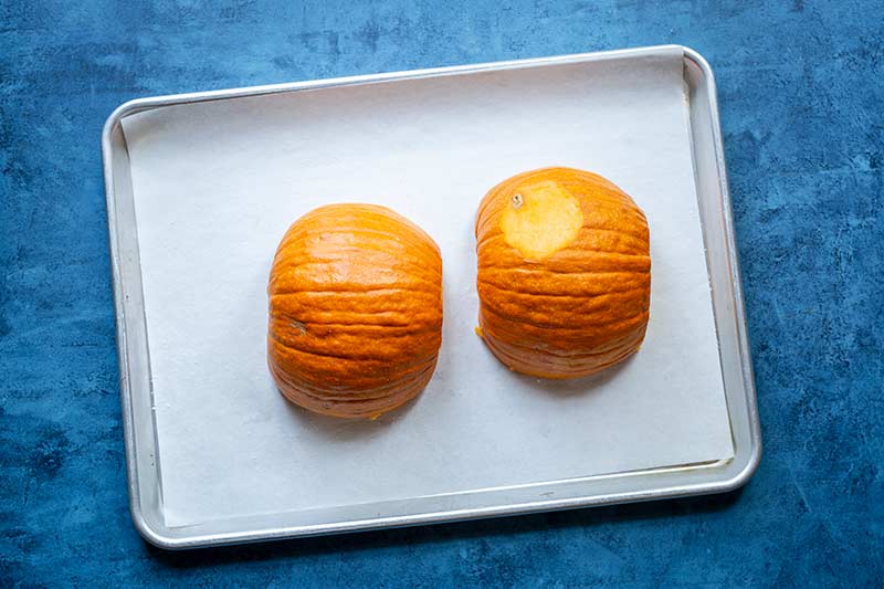 Two seeded pumpkin halves lying flesh side down on a sheet pan lined with parchment paper