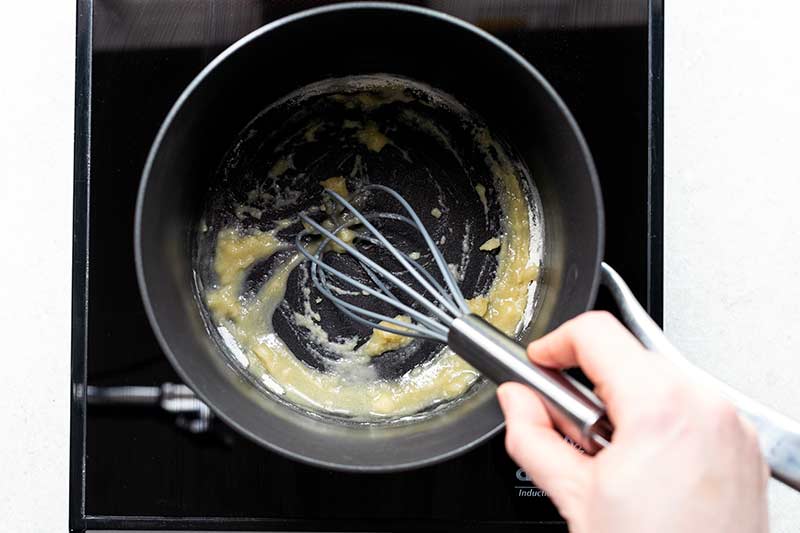 woman's hand holding whisk, making a roux with butter and flour in a saucepan
