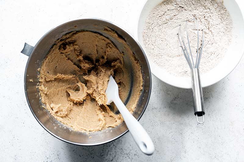 Butter and sugar creamed in a mixing bowl next to dry ingredients whisked together in a separate bowl