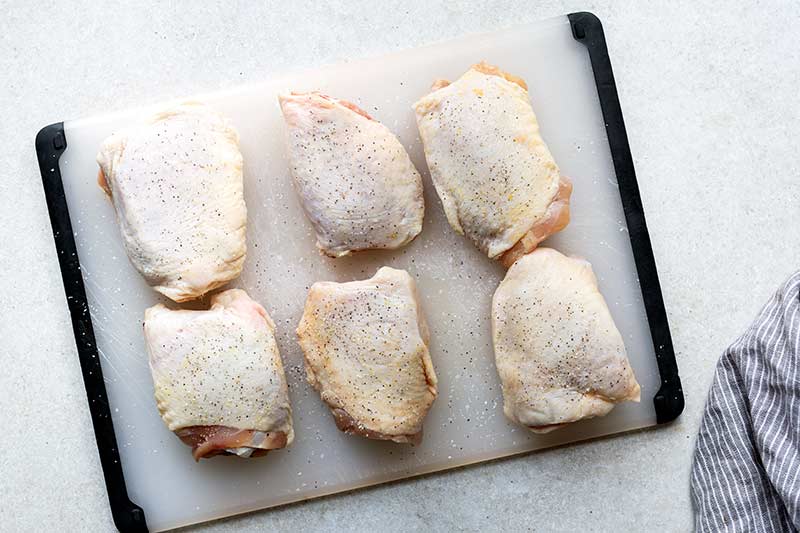 Raw, bone-in skin on chicken thighs on a cutting board