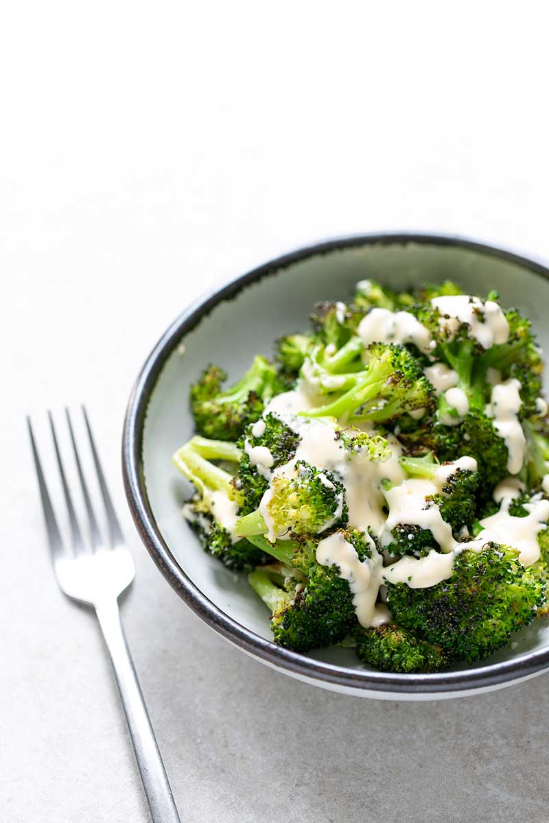 Roasted broccoli with cheese sauce in a bowl next to a fork