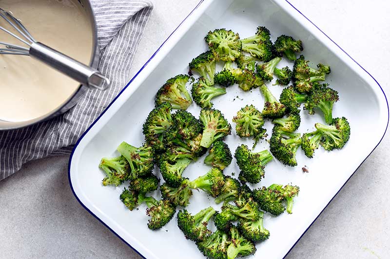  pan of roasted broccoli next to homemade cheese sauce