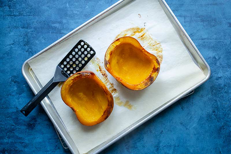 Roasted pumpkin halves flesh side up on a sheet pan lined with parchment paper