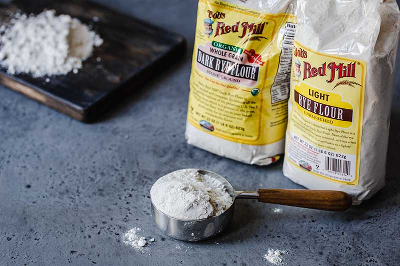 dark and light rye flour bags next to flour in measuring cup