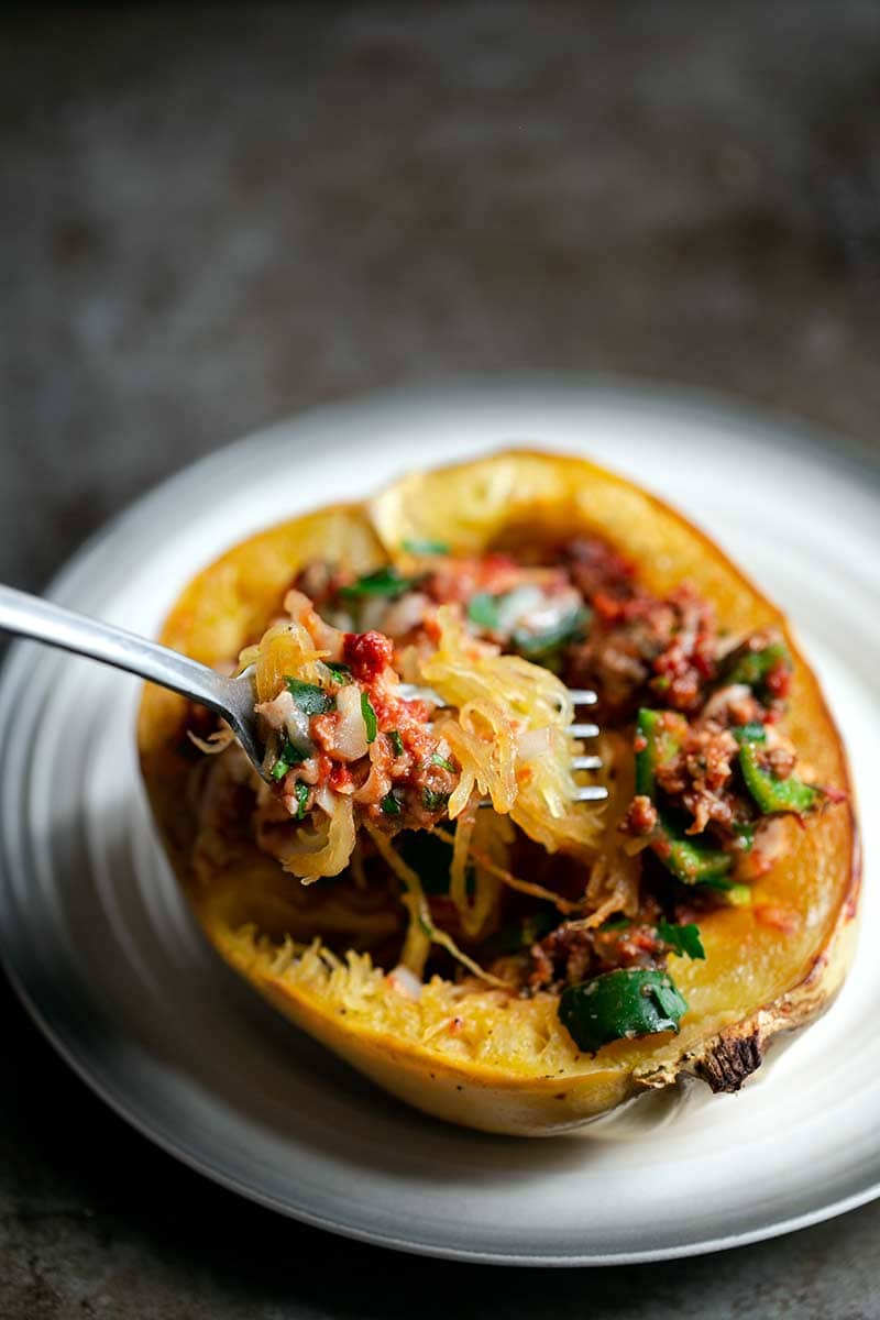 A Baked Spaghetti Squash Boat on a plate with a fork scooping up some of the filling
