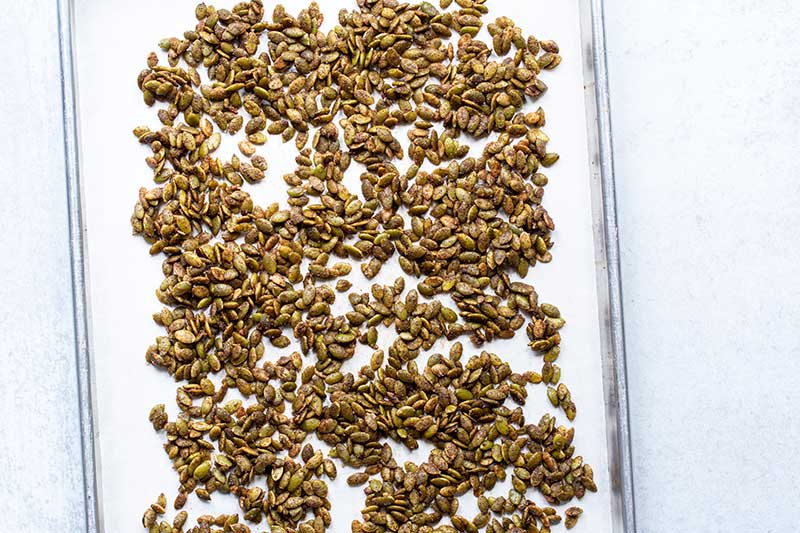 A parchment-lined sheet pan topped with raw pumpkin seeds tossed in remaining ingredients