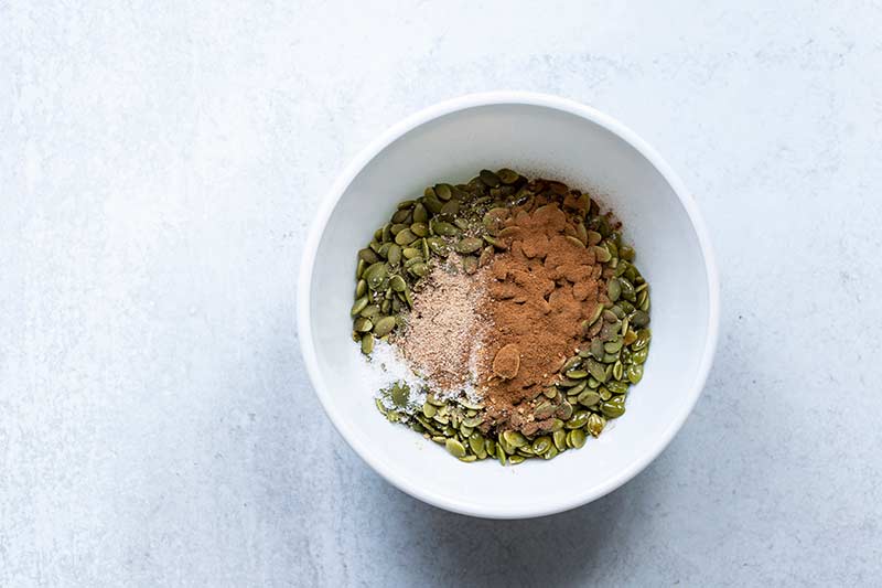 Raw pumpkin seeds in a bowl topped with spices