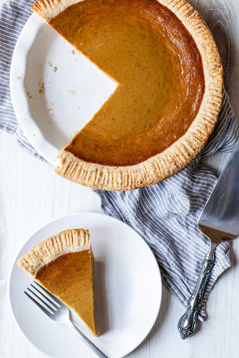 Overhead photo of pumpkin pie from scratch in a pie dish next to a slice of pumpkin pie