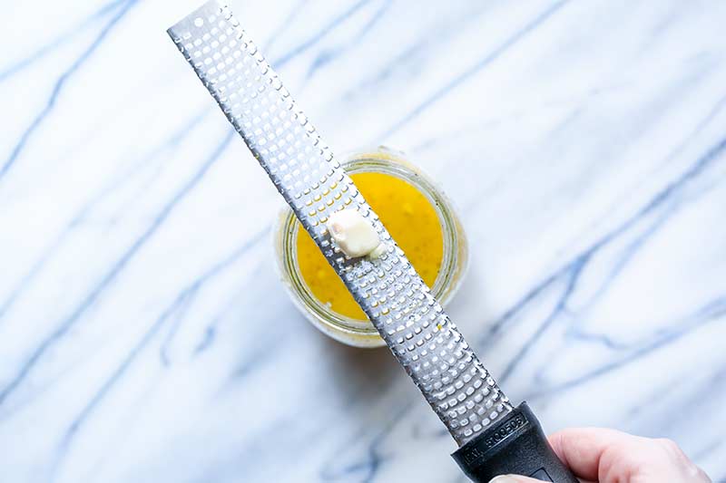 garlic clove being grated with microplane zester into dressing