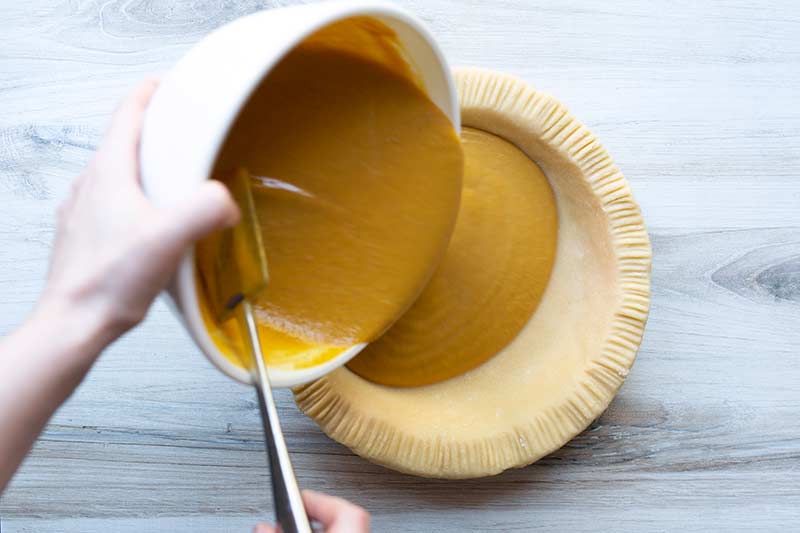 action shot pouring pumpkin pie filling into pie crust.