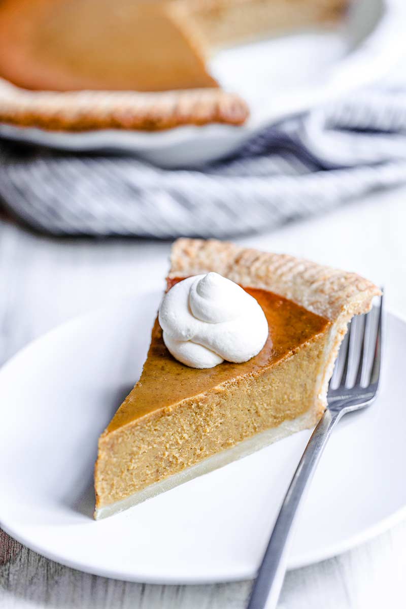 a slice of homemade pumpkin pie from scratch topped with whipped cream.
