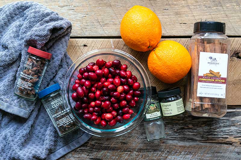 Ingredients for stovetop potpourri spread out on a wooden table, including cranberries, oranges and whole spices