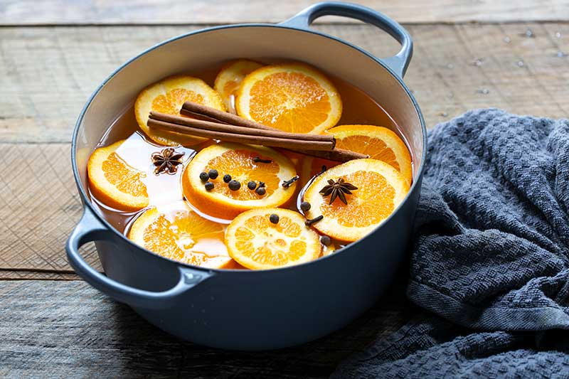 Orange slices and cinnamon sticks in a Dutch oven filled with water