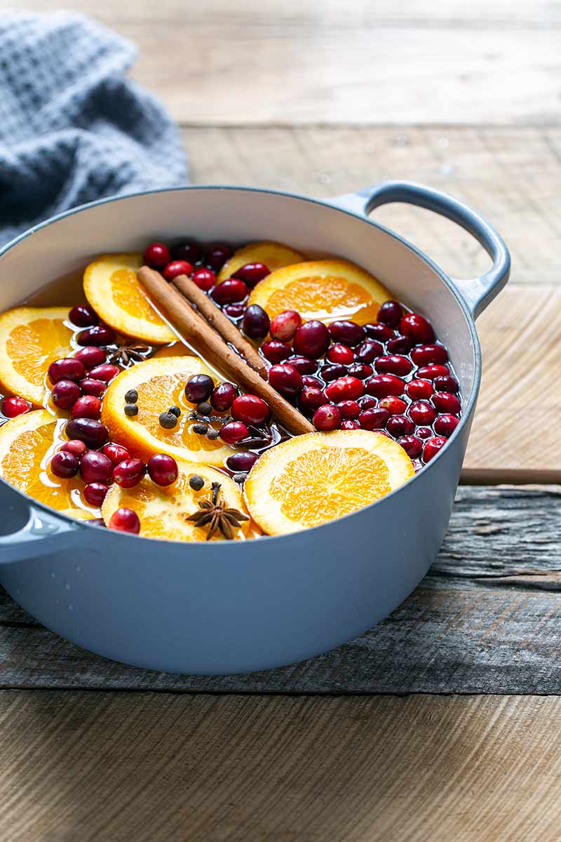 Stovetop potpourri recipe ingredients in a Dutch oven, including orange slices and cinnamon sticks