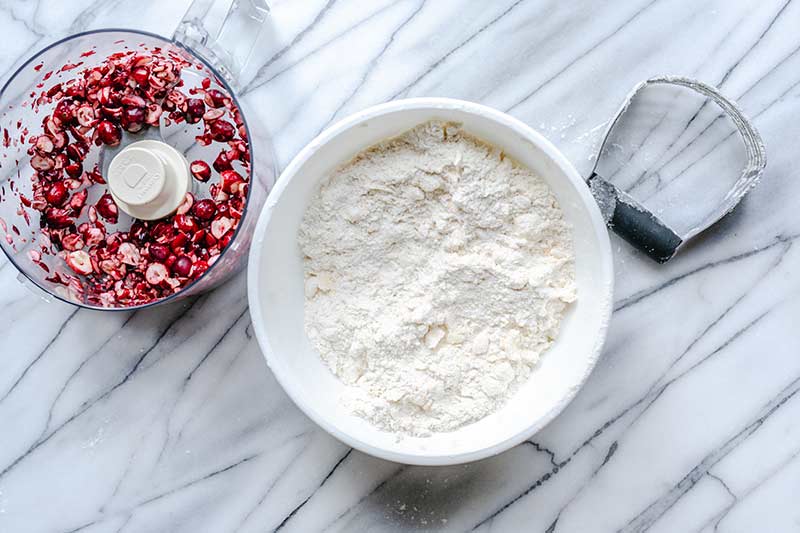 Scone ingredients in a bowl next to a food processor with chopped cranberries.