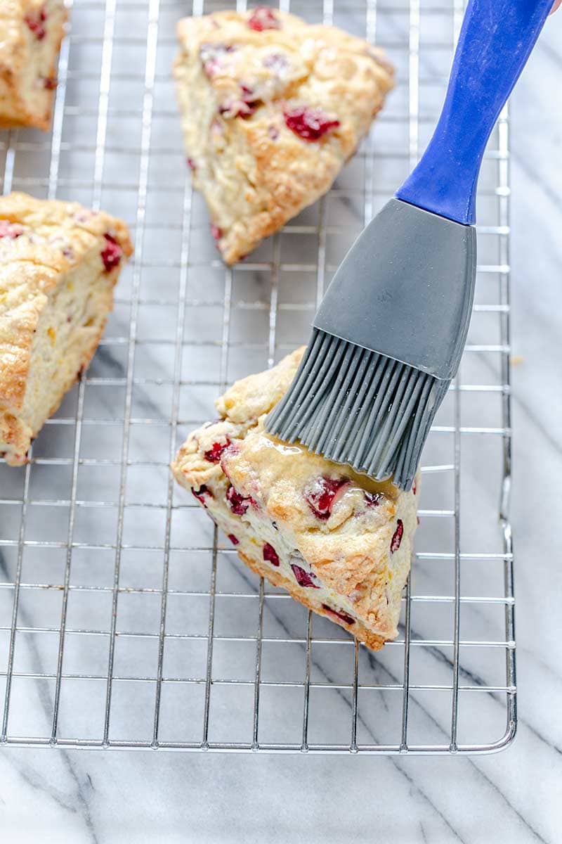A pastry brush brushing glaze onto cranberry orange scones recipe.