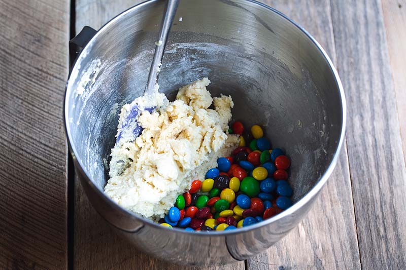 Cookie dough and M&Ms in a stand mixer with a spatula