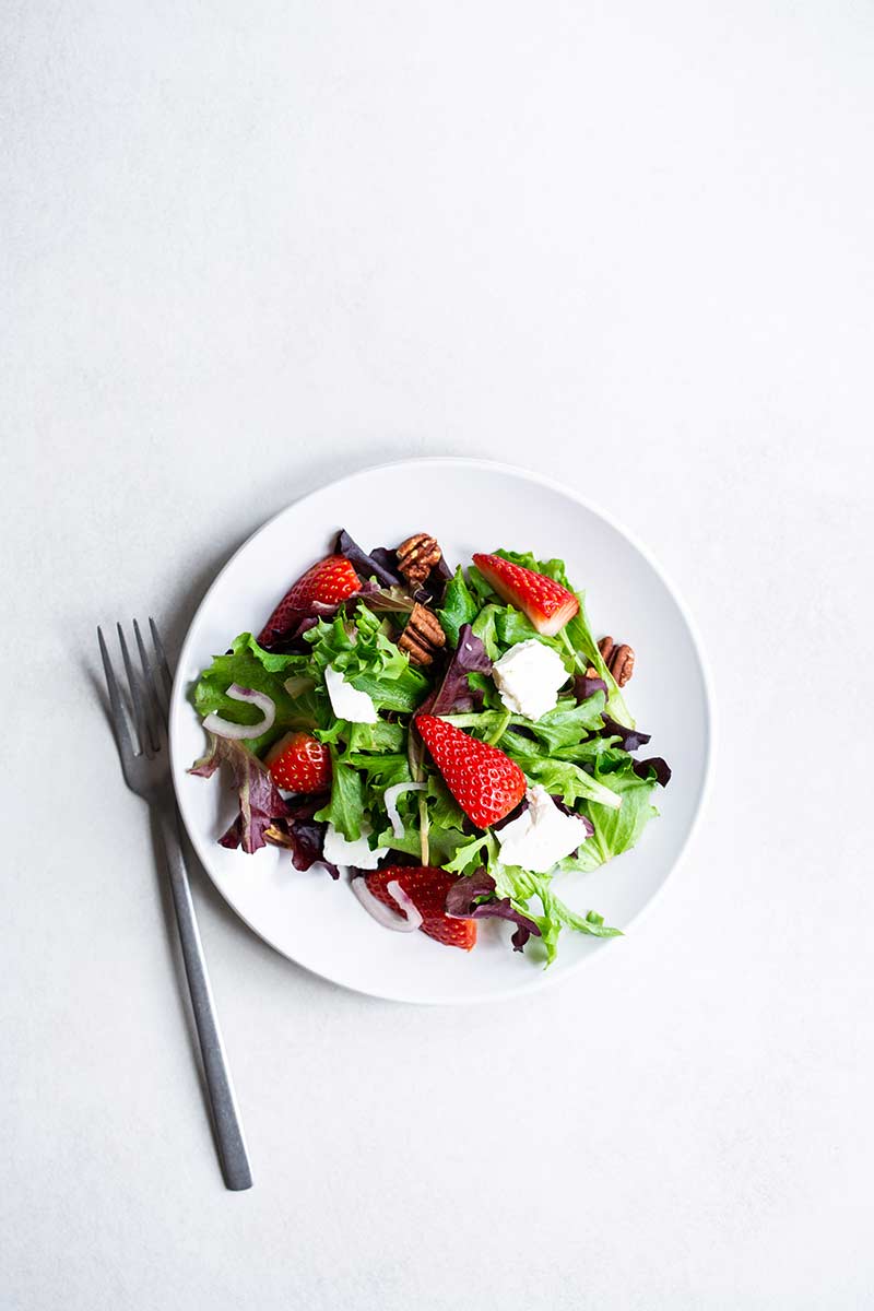 Strawberry salad topped with pickled shallots and feta cheese on a white plate.