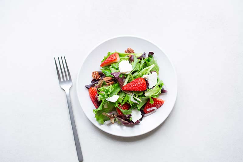 Mixed greens with strawberries, pecans and feta on a plate with a fork.