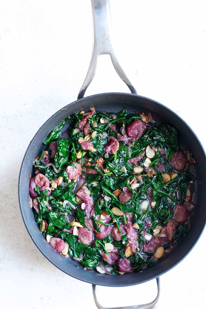 Sautéed spinach with grapes and almonds in a skillet shot from overhead