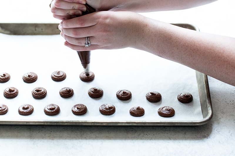 Piping macaron batter onto a parchment lined sheet pan