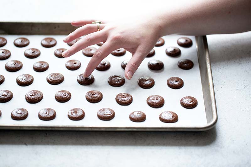 Using fingers to dab water on top of the unbaked chocolate macarons to smooth out the top