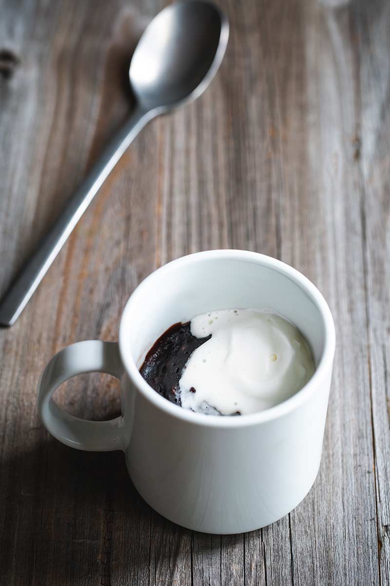 brownie in a mug topped with whipped cream next to a spoon