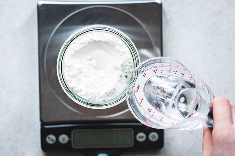  water poured into a jar with flour set on a digital scale