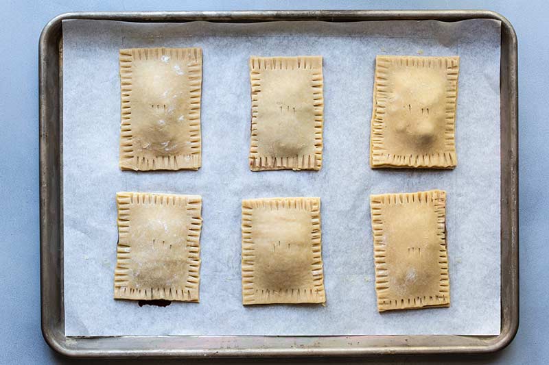 Six uncooked tarts on a baking sheet lined with parchment