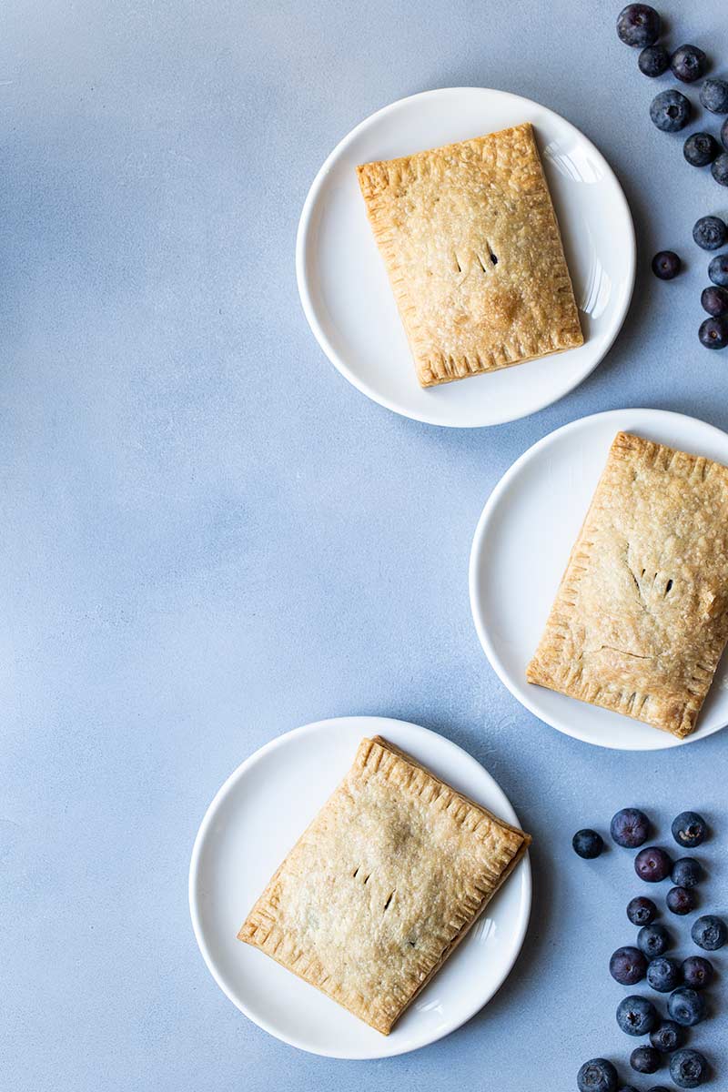 Three blueberry pop tarts on plates, surrounded by blueberries