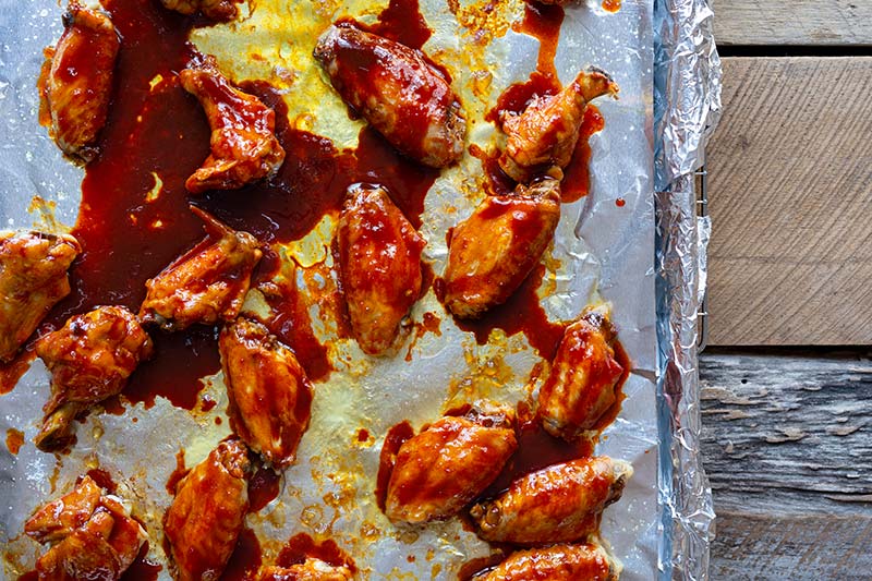 Chicken wings tossed with gochujang on a sheet pan lined with foil.
